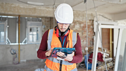 Young hispanic man builder using touchpad at construction site