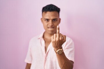 Young hispanic man standing over pink background showing middle finger, impolite and rude fuck off expression