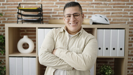 Young hispanic man business worker standing with arms crossed gesture at office