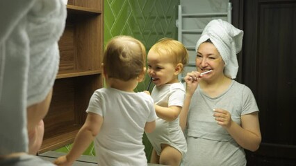 Female person and child brush teeth looking in large mirror in bathroom. Positive baby rejoices in reflection. Routine procedure concept