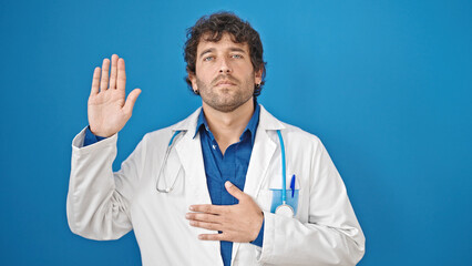 Young hispanic man doctor making an oath with hand on chest over isolated blue background
