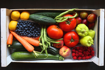 Wooden crate full of healthy seasonal fruit and vegetable. Top view, dark background.