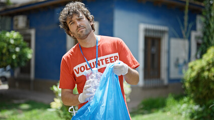 Young hispanic man activist wearing volunteer uniform recycling plastic bottles at park