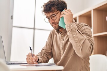 Young man business worker talking on smartphone writing on notebook at office
