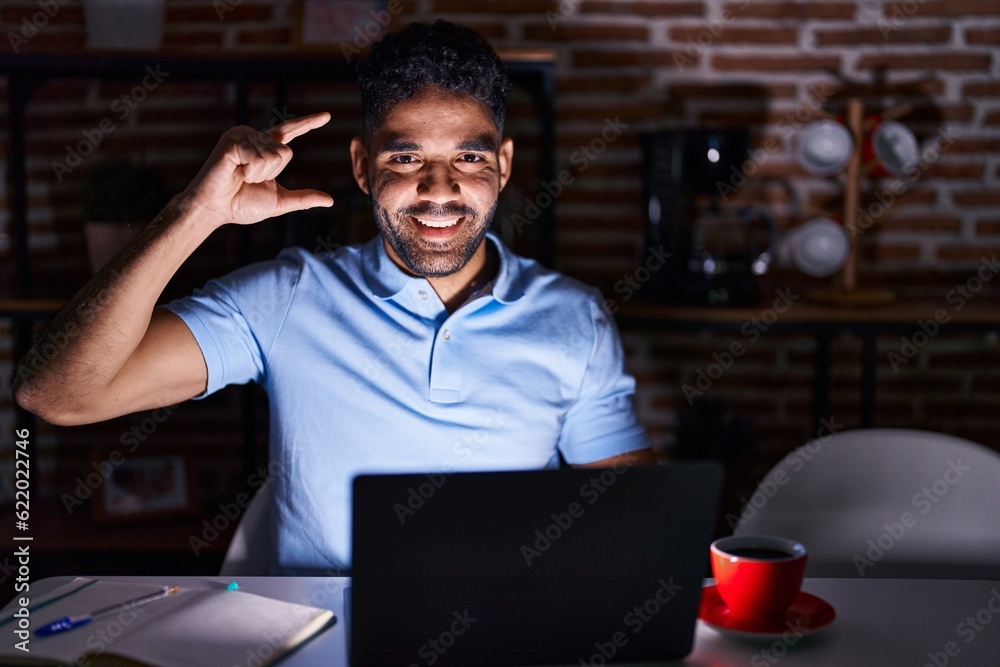 Poster hispanic man with beard using laptop at night smiling and confident gesturing with hand doing small 