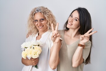 Mother and daughter holding bouquet of white flowers smiling looking to the camera showing fingers...