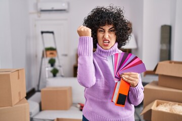 Young brunette woman with curly hair choosing color of new house wall annoyed and frustrated...