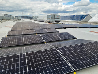 Solar panels installed on a roof of a large industrial building or a warehouse. Industrial buildings in the background.
