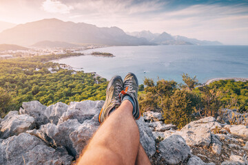 Hiker legs with trekking shoes on top of the canyon cliff with view of Kemer sea coast. Outdoors activity and skyrunning concept