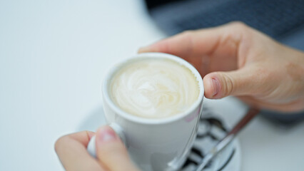 Young blonde woman holding cup of coffee sitting on table at coffee shop terrace