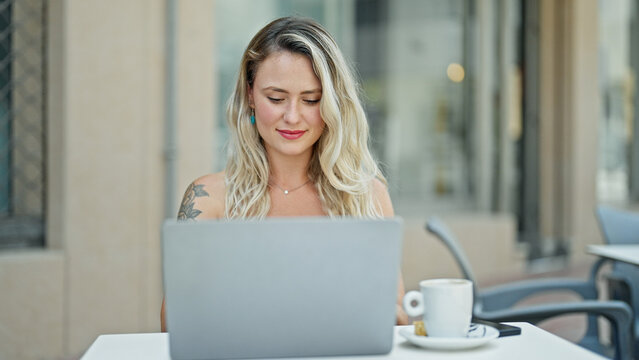 Young blonde woman using laptop sitting on table at coffee shop terrace