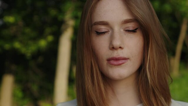 Push out scene of a beautiful red haired woman with freckles looking at camera against a forest.