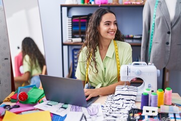 Young beautiful hispanic woman tailor smiling confident using laptop at clothing factory