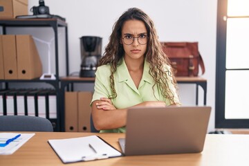 Young hispanic woman working at the office wearing glasses skeptic and nervous, disapproving expression on face with crossed arms. negative person.