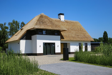 Modern new detached family house with white facade and traditional thatched roof, spacious driveway in rural setting - Netherlands