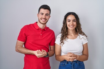 Young hispanic couple standing over isolated background with hands together and crossed fingers smiling relaxed and cheerful. success and optimistic