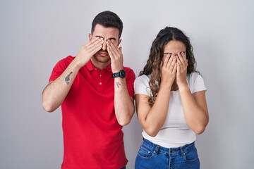 Young hispanic couple standing over isolated background rubbing eyes for fatigue and headache,...