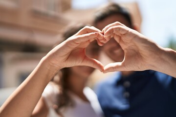 Young hispanic couple smiling confident doing heart gesture with hands at street