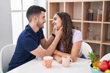 Young hispanic couple drinking coffee sitting on table at home