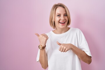 Young caucasian woman standing over pink background pointing to the back behind with hand and thumbs up, smiling confident