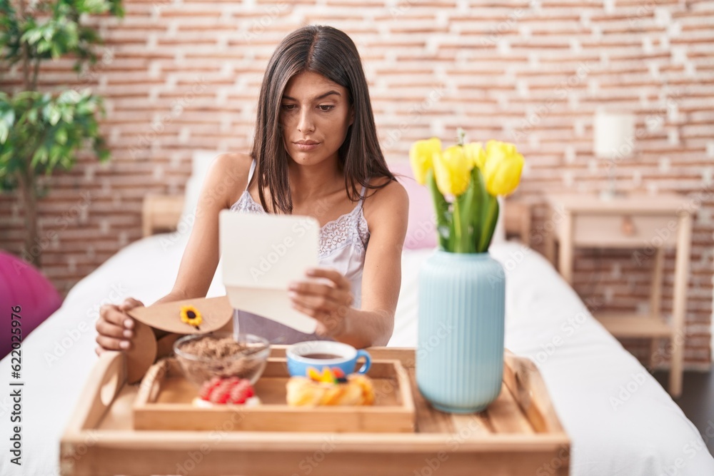 Poster brunette young woman eating breakfast in the bed reading a letter skeptic and nervous, frowning upse