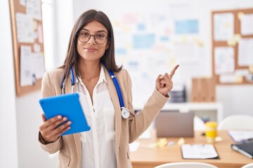 Brunette young woman working at the office wearing stethoscope smiling happy pointing with hand and...