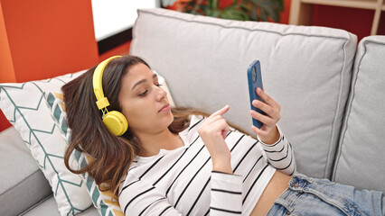 Young beautiful hispanic woman listening to music lying on sofa at home