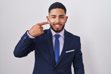 Young hispanic man wearing business suit and tie pointing with hand finger to face and nose, smiling cheerful. beauty concept