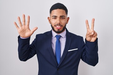 Young hispanic man wearing business suit and tie showing and pointing up with fingers number seven while smiling confident and happy.