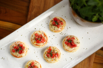 Deliciosas mini pizzas de queijo mussarela, tomates e manjericão, perfeitas para saborear em um evento especial.