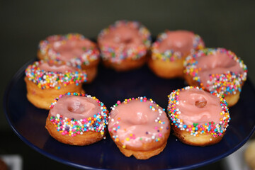 Donuts de creme cor-de-rosa cobertos com confetes coloridos, uma delícia irresistível na mesa de doces da festa infantil.