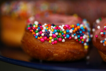 Donuts de creme cor-de-rosa cobertos com confetes coloridos, uma delícia irresistível na mesa de doces da festa infantil.