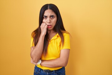 Young arab woman standing over yellow background looking stressed and nervous with hands on mouth biting nails. anxiety problem.