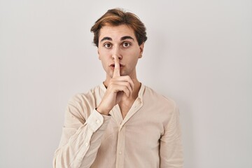 Young man standing over isolated background asking to be quiet with finger on lips. silence and secret concept.