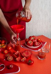 Woman in red pouring tomatoes juice into glass bottle - 622028704
