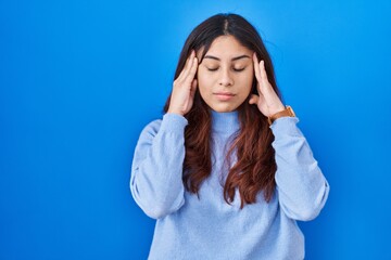 Fototapeta premium Hispanic young woman standing over blue background with hand on head, headache because stress. suffering migraine.
