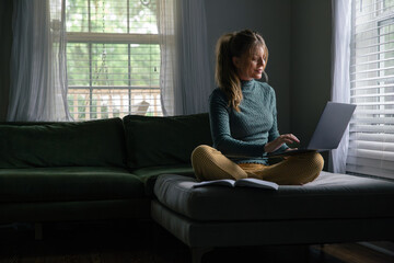 Business Woman Work from Home on Laptop Computer, Remote Employee Worker, Sitting in Living Room of House. Looking at screen with grin.