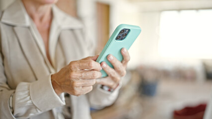 Middle age blonde woman architect using smartphone at construction site