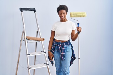 African american woman holding roller painter winking looking at the camera with sexy expression,...