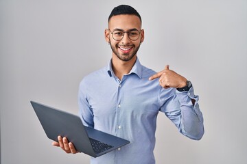 Young hispanic man working using computer laptop looking confident with smile on face, pointing oneself with fingers proud and happy.