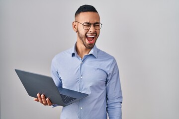 Young hispanic man working using computer laptop angry and mad screaming frustrated and furious, shouting with anger. rage and aggressive concept.