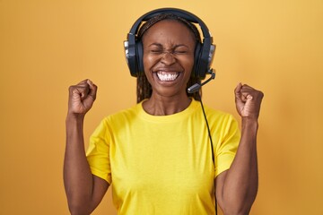African american woman listening to music using headphones excited for success with arms raised and...