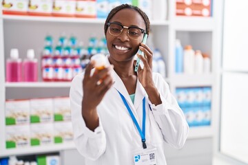 African american woman pharmacist holding pills bottle talking on smartphone at pharmacy