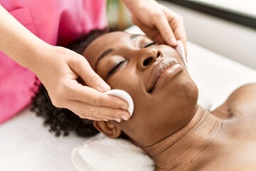 Fototapeta na wymiar African american woman lying on massage table having facial treatment at beauty salon