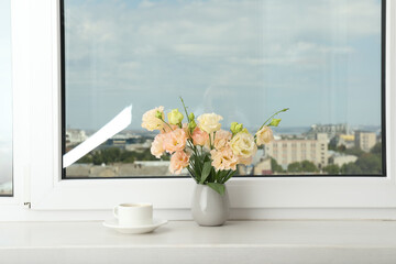 A pot of coffee and a vase of flowers on the windowsill with a view of the city