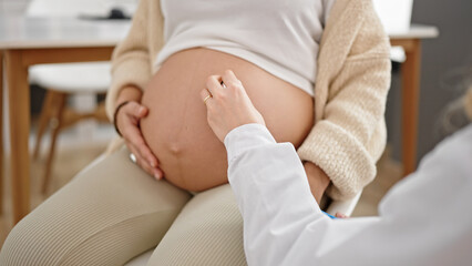 Young pregnant woman gynecologist and patient examining belly with stethoscope at clinic