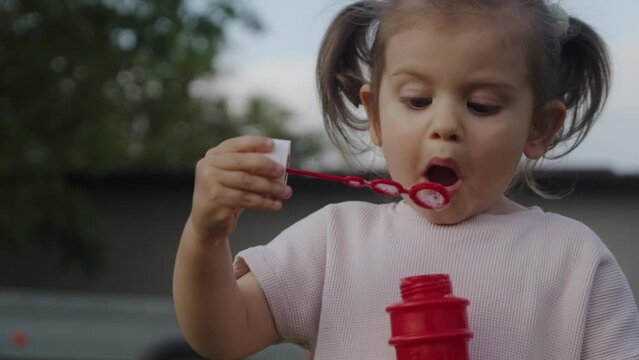 Beautiful little girl doing soap balloons outside at home.