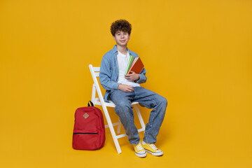 A happy teenager sits on a chair, on a yellow background