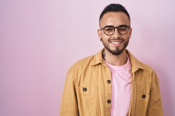Young hispanic man standing over pink background winking looking at the camera with sexy expression, cheerful and happy face.