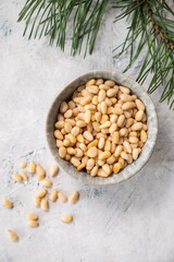 Pine nuts in a bowl  and scattered on a white texture background with branches of pine needles close up. The concept of natural, organic and healthy superfoods